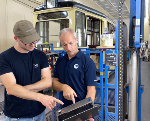 2 Männer mit blauen Schirt schauten in ein Tablet